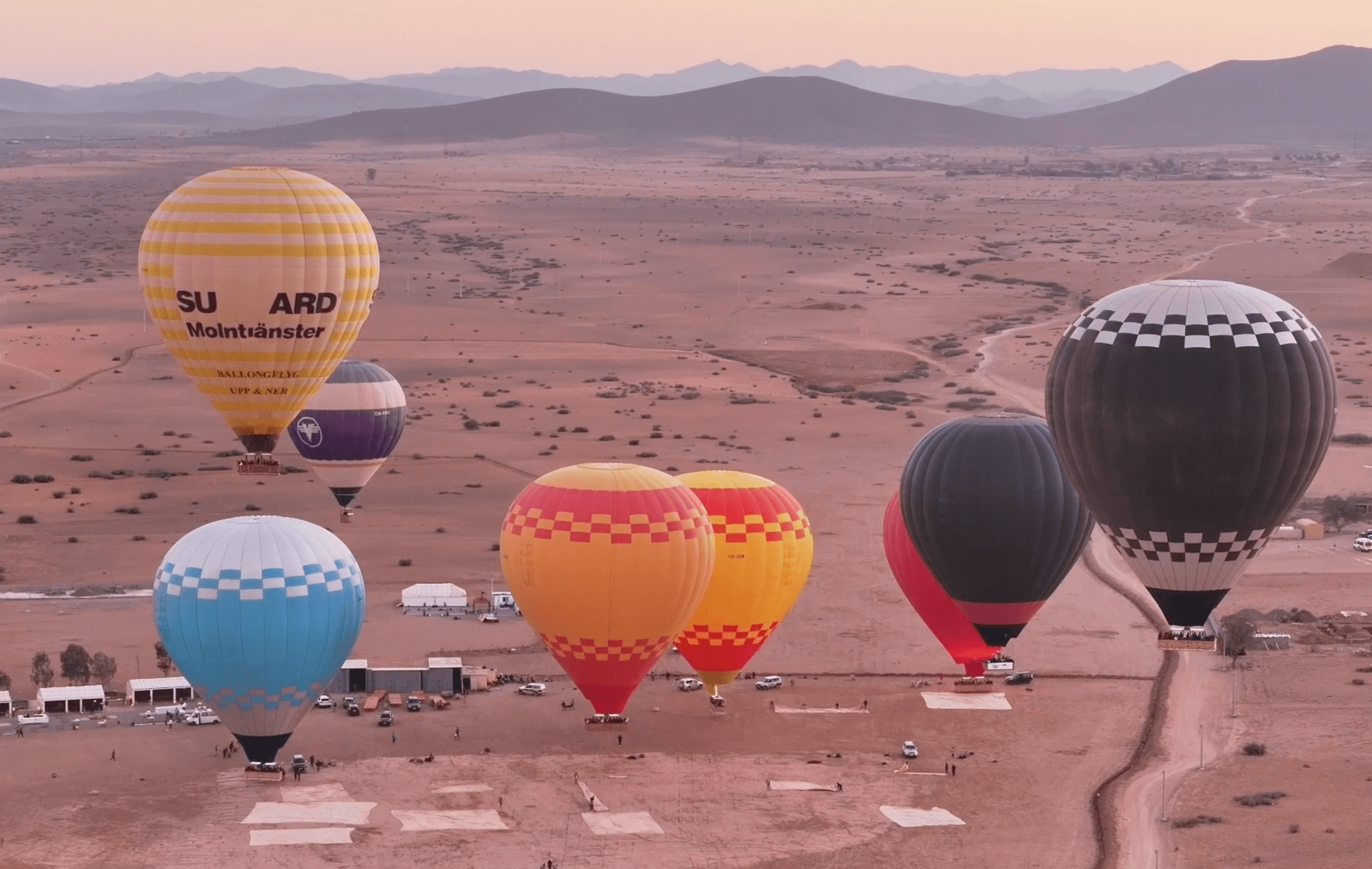 Multiple hot air balloons inflated across desert launch field at soft sunrise light.