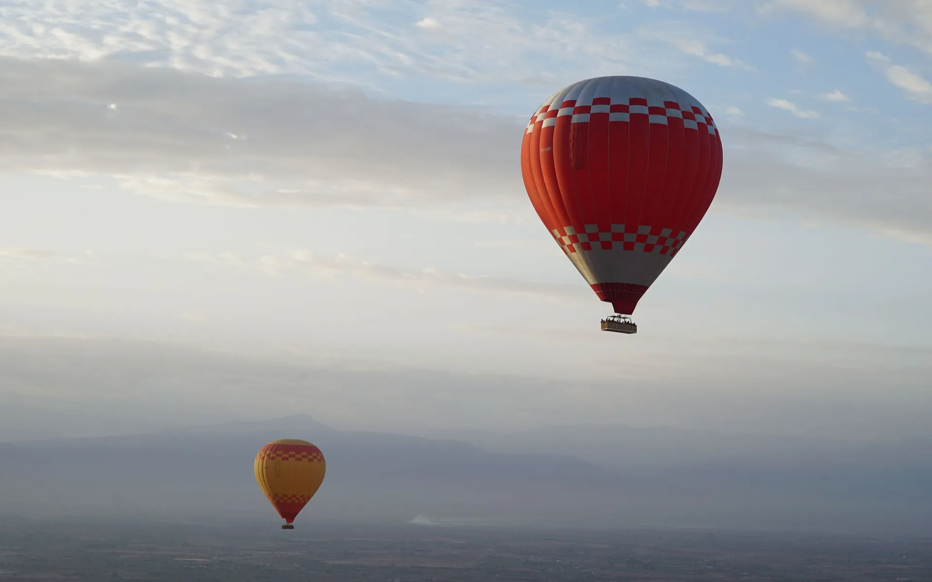 Two hot air balloons floating over misty valley, soft sunrise tones, distant mountain silhouettes