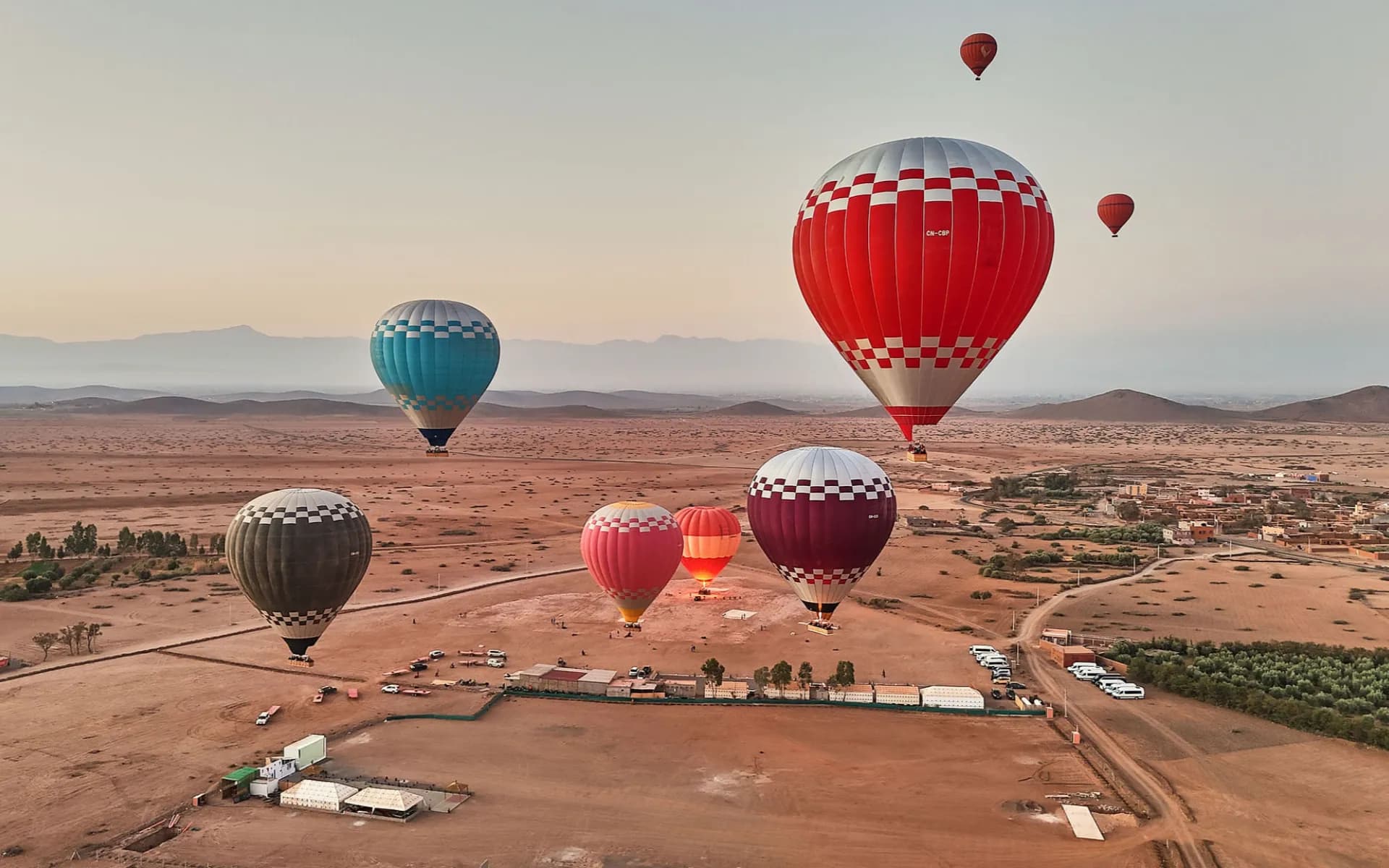 Aerial view of multiple hot air balloons lifting off from desert launch site, calm morning